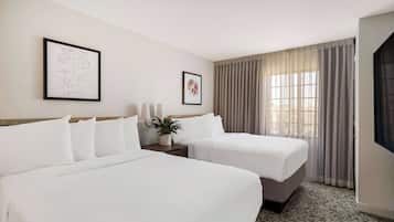 A hotel room with two beds, a potted plant, and artwork on the walls.