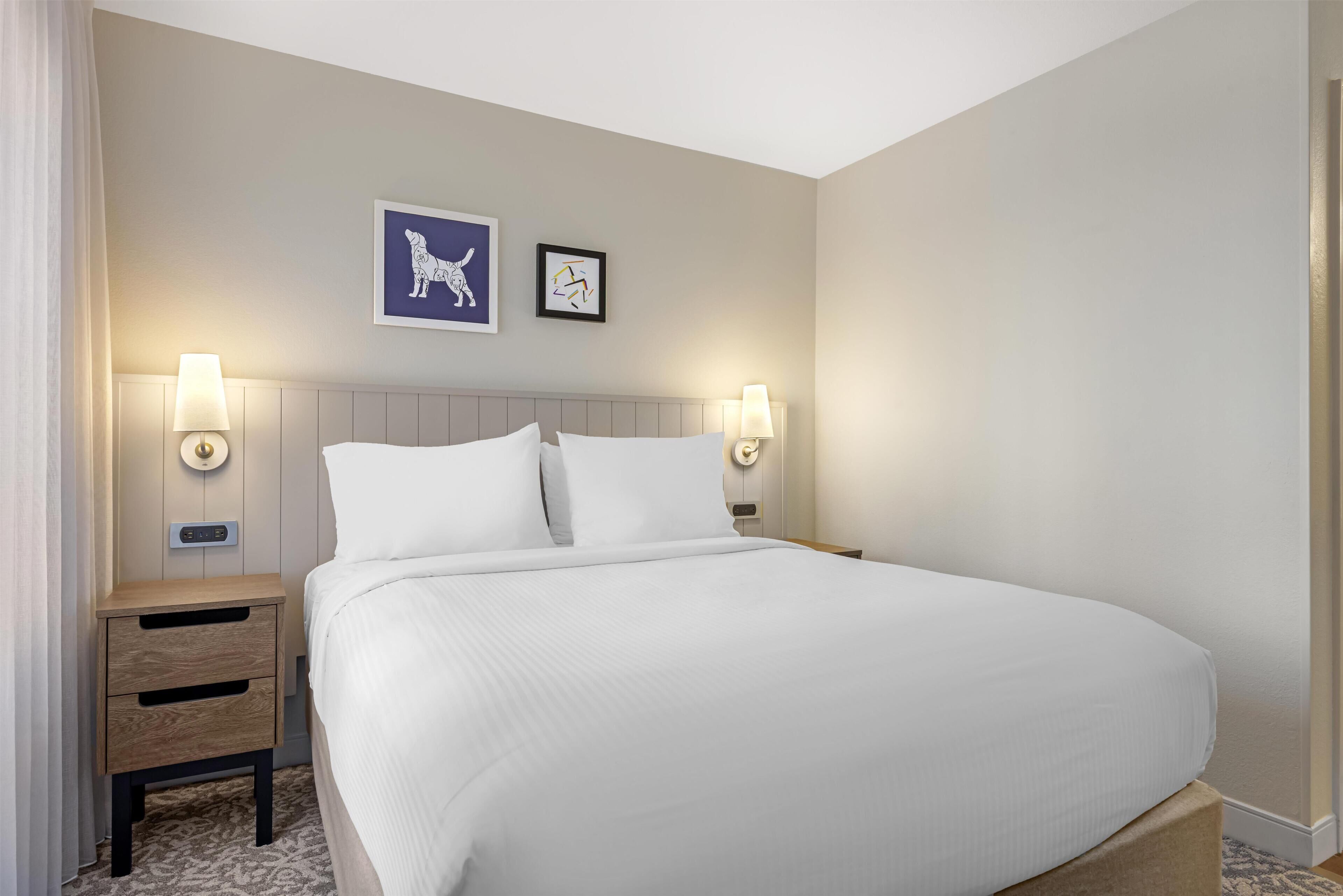 Ein Hotelzimmer mit einem großen Bett, zwei Nachttischen, einer Wanduhr und zwei Wandleuchten.