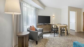 A modern living room with a sofa, a coffee table, a TV, and a dining area with chairs and a table.