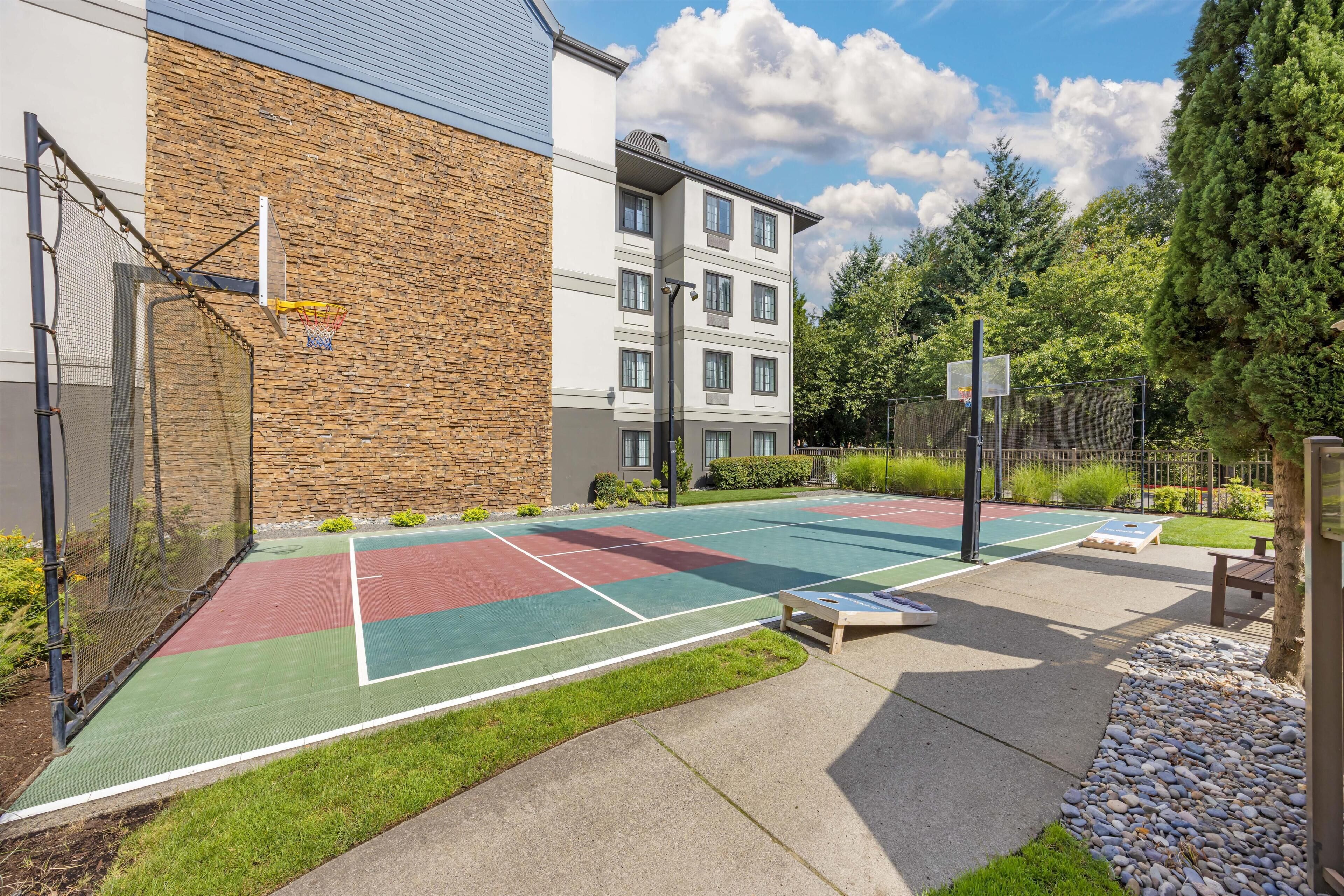 An outdoor basketball court with a stone wall and a building in the background.