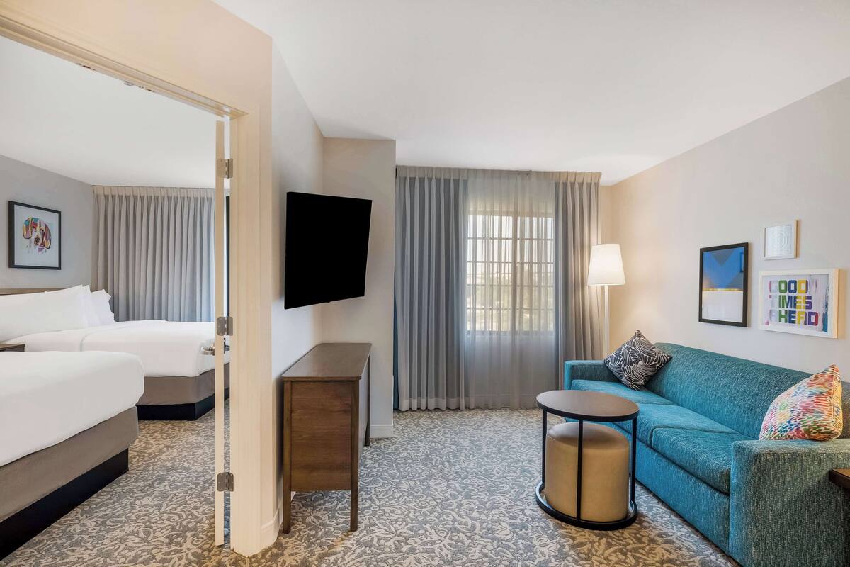 A hotel room with two beds, a sofa, a TV, a lamp, and a patterned carpet.