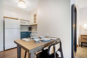 A modern kitchen with white cabinets, a built-in microwave, and a coffee maker. A dining table with plates, glasses, and cutlery is set for four. - Sonesta ES Suites Portland Vancouver 41st Street (Vancouver)