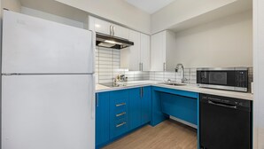 Una cocina compacta con armarios blancos, encimera azul, microondas y lavavajillas.