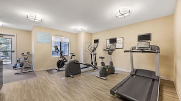 Un gimnasio con cintas de correr, bicicletas estáticas y pesas sueltas.