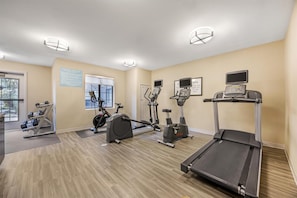 Un gimnasio con cintas de correr, bicicletas estáticas y pesas sueltas.