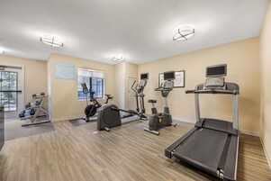 Un gimnasio con cintas de correr, bicicletas estáticas y pesas sueltas.