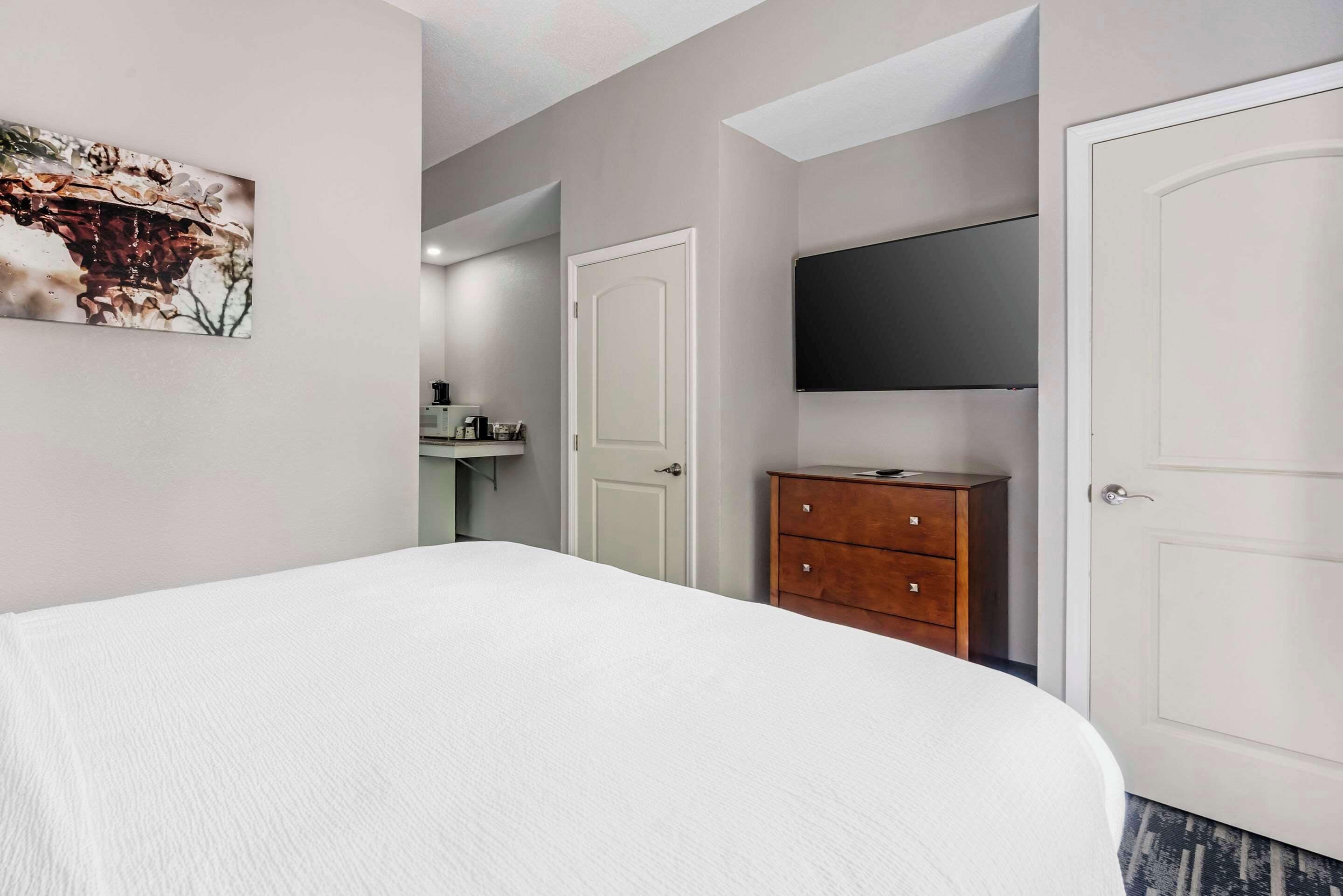 Quarto com uma cama, cómoda de madeira, televisão e uma porta.
