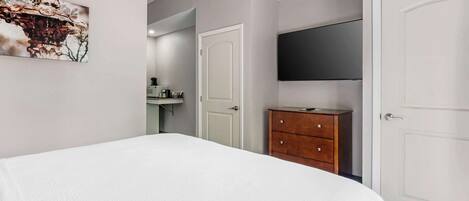 A bedroom with a bed, a wooden dresser, a television, and a door.