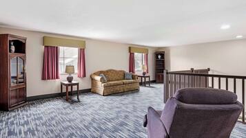 A hotel room with a patterned carpet, a sofa, a chair, a cabinet, and a window with curtains.
