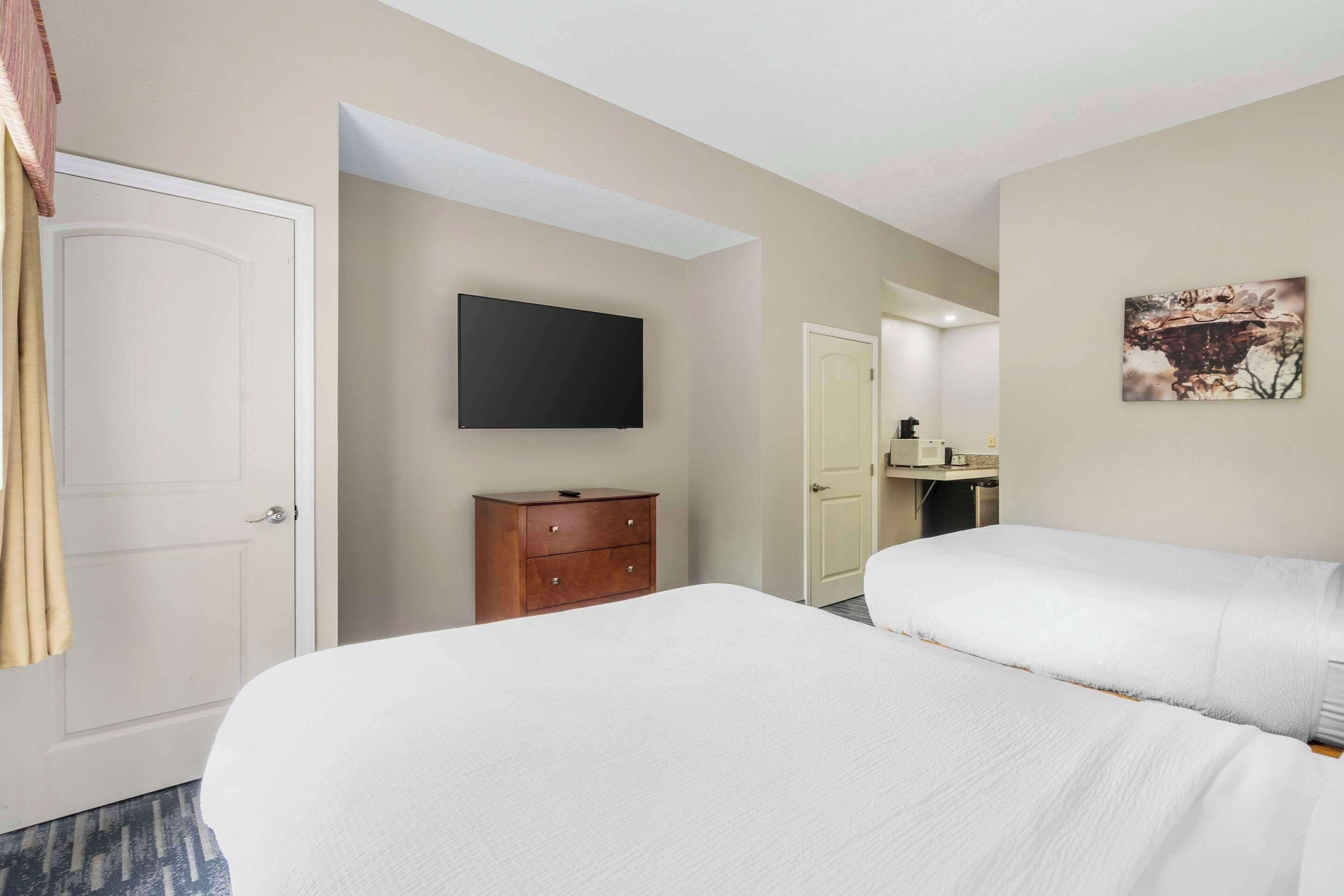 Habitación de hotel con dos camas, un televisor, un aparador de madera y un cuadro en la pared.