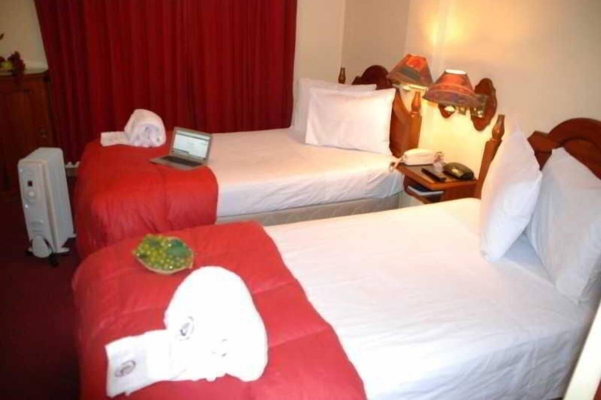 A hotel room with two beds, a laptop on one bed, a lamp on the nightstand, and a red curtain in the background.