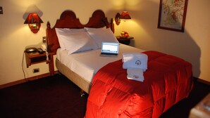 Habitación de hotel con una cama, un ordenador portátil sobre la cama, una mesita de noche con una lámpara, un teléfono y un frutero.