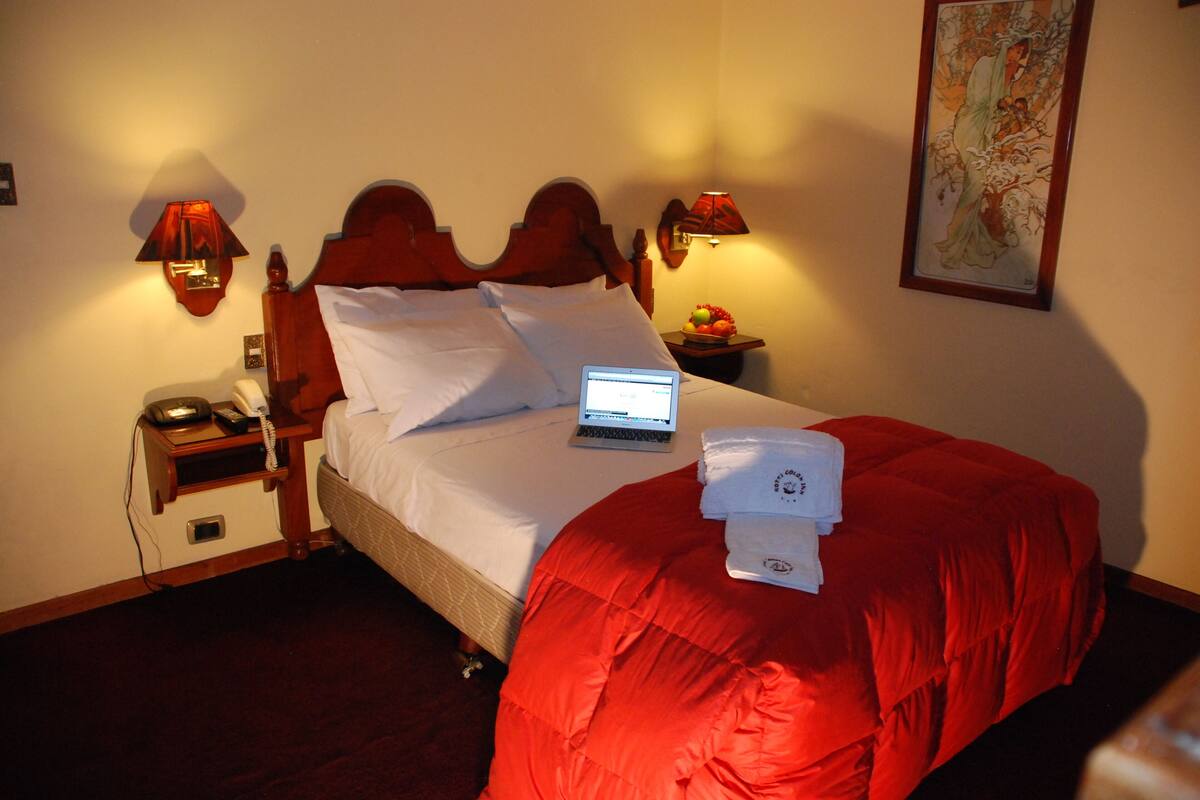 A hotel room with a bed, a laptop on the bed, a bedside table with a lamp, a telephone, and a fruit bowl.