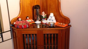 Un mueble de madera con tapa de cristal, que contiene varios utensilios de cocina como una cafetera, platos y una pila de tazas.