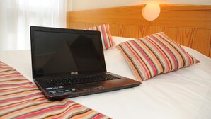 A laptop on a bed with striped bedding and a wooden headboard. - Hotel Kiotel Lyon Bron Eurexpo (Bron)