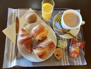 A breakfast tray with croissants, a kiwi, a glass of orange juice, a cup of coffee, and packaged snacks. - Hotel Kiotel Lyon Bron Eurexpo (Bron)