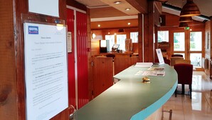 A hotel reception area with a wooden interior, a reception desk, and a sign indicating English is spoken. - Hotel Kiotel Lyon Bron Eurexpo (Bron)
