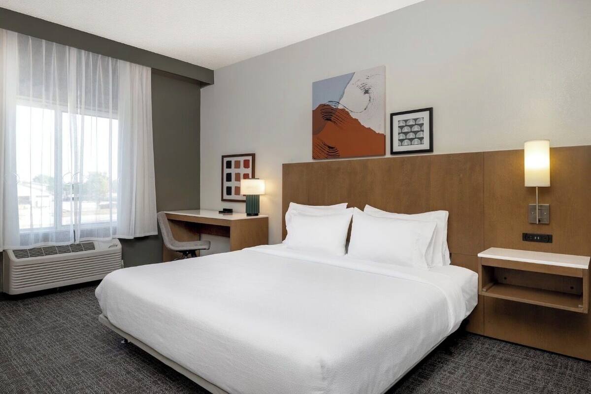 Une chambre d’hôtel avec un grand lit, un bureau, une chaise, une lampe et des œuvres d’art accrochées au mur.