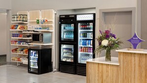 Un espace équipé de bornes de libre-service avec des distributeurs de boissons réfrigérées, des étagères de snacks et un arrangement floral sur un comptoir.