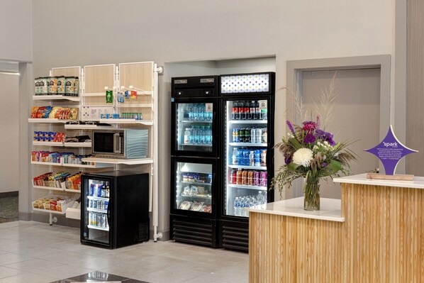 A self-service kiosk area with refrigerated beverage dispensers, snack shelves, and a floral arrangement on a counter.