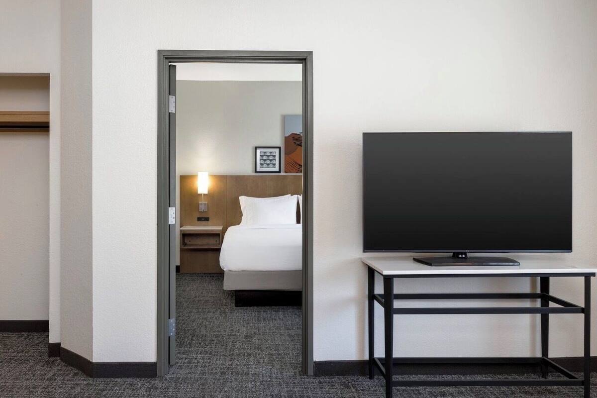Une chambre d’hôtel avec un lit, un téléviseur posé sur un meuble et une table de chevet avec une lampe.