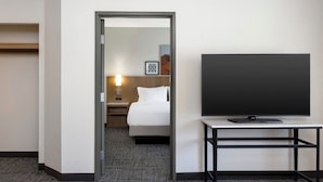 Une chambre d’hôtel avec un lit, un téléviseur posé sur un meuble et une table de chevet avec une lampe.