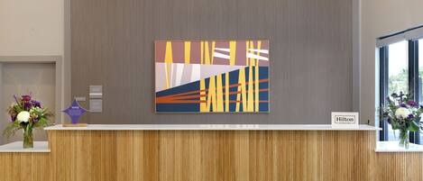 Un mostrador de recepción de hotel con diseño moderno, una gran obra de arte abstracta sobre él y un cartel que indica 'Hilton Honors'.