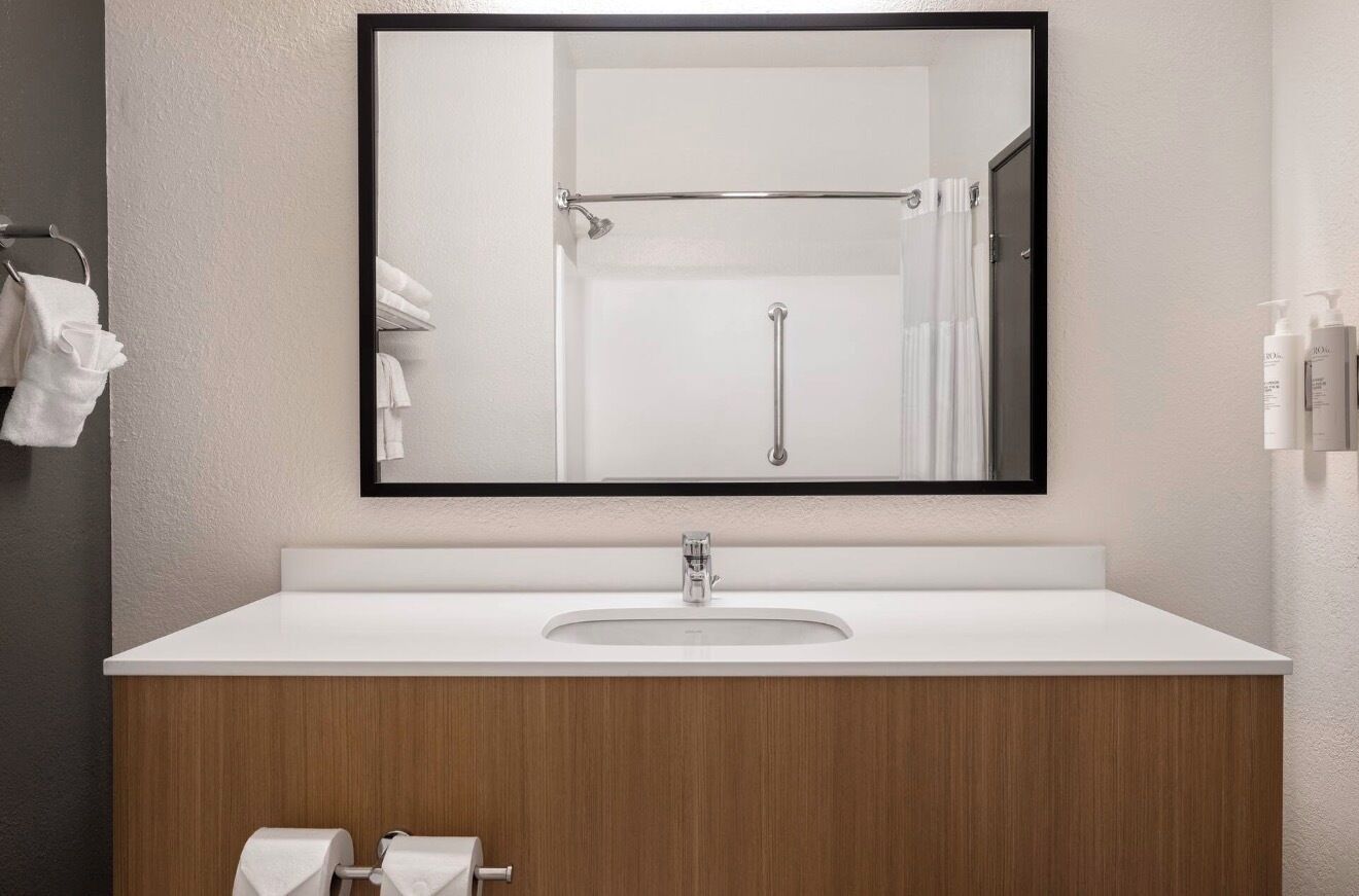 Une salle de bain moderne avec un lavabo blanc, un meuble-lavabo en bois et un grand miroir.