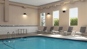 Une piscine dotée de chaises longues et de tables, de grandes fenêtres offrant une vue dégagée et d’un sol carrelé.
