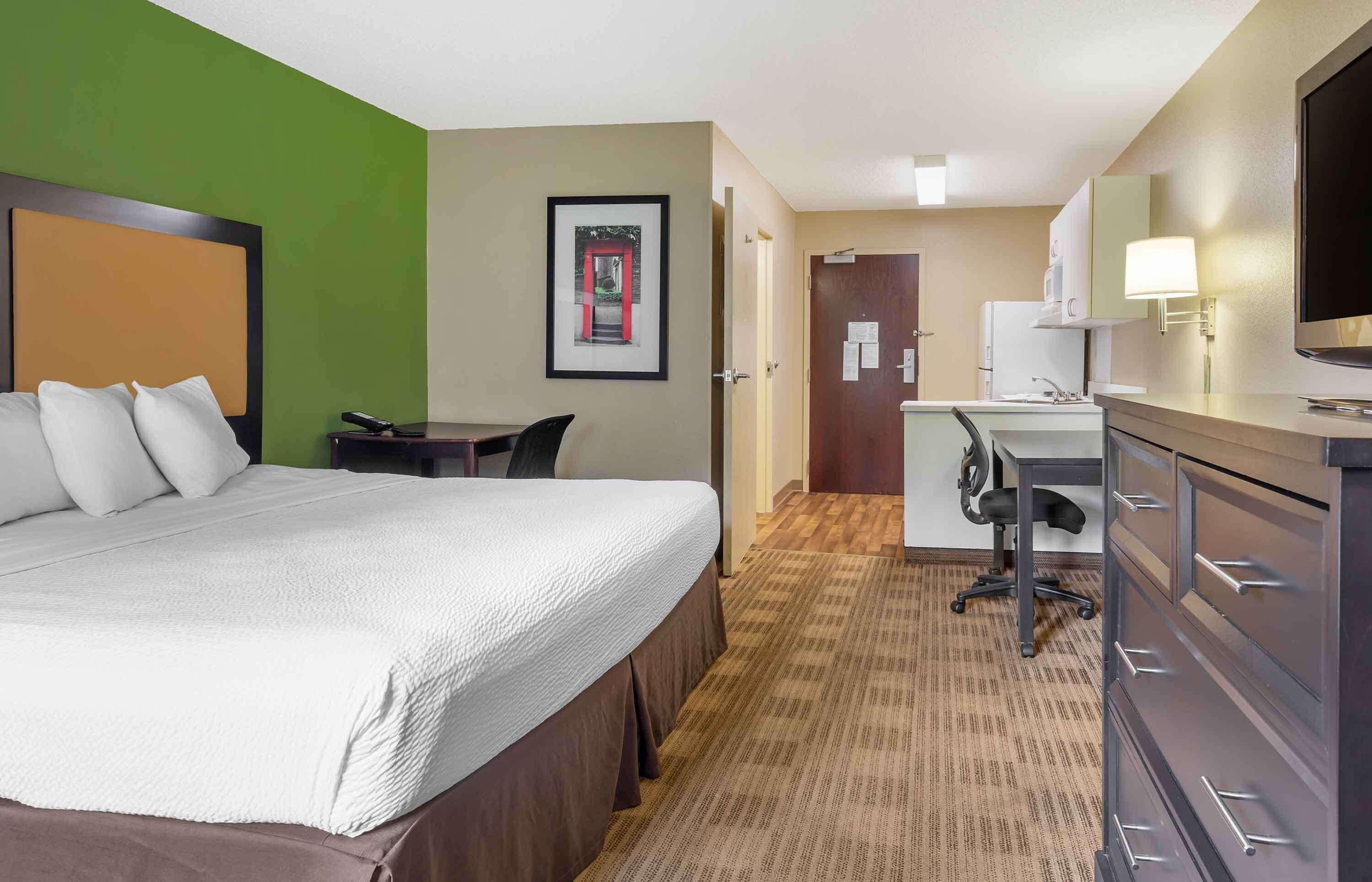 A hotel room with a large bed, a desk, a chair, a television, and a wardrobe.
