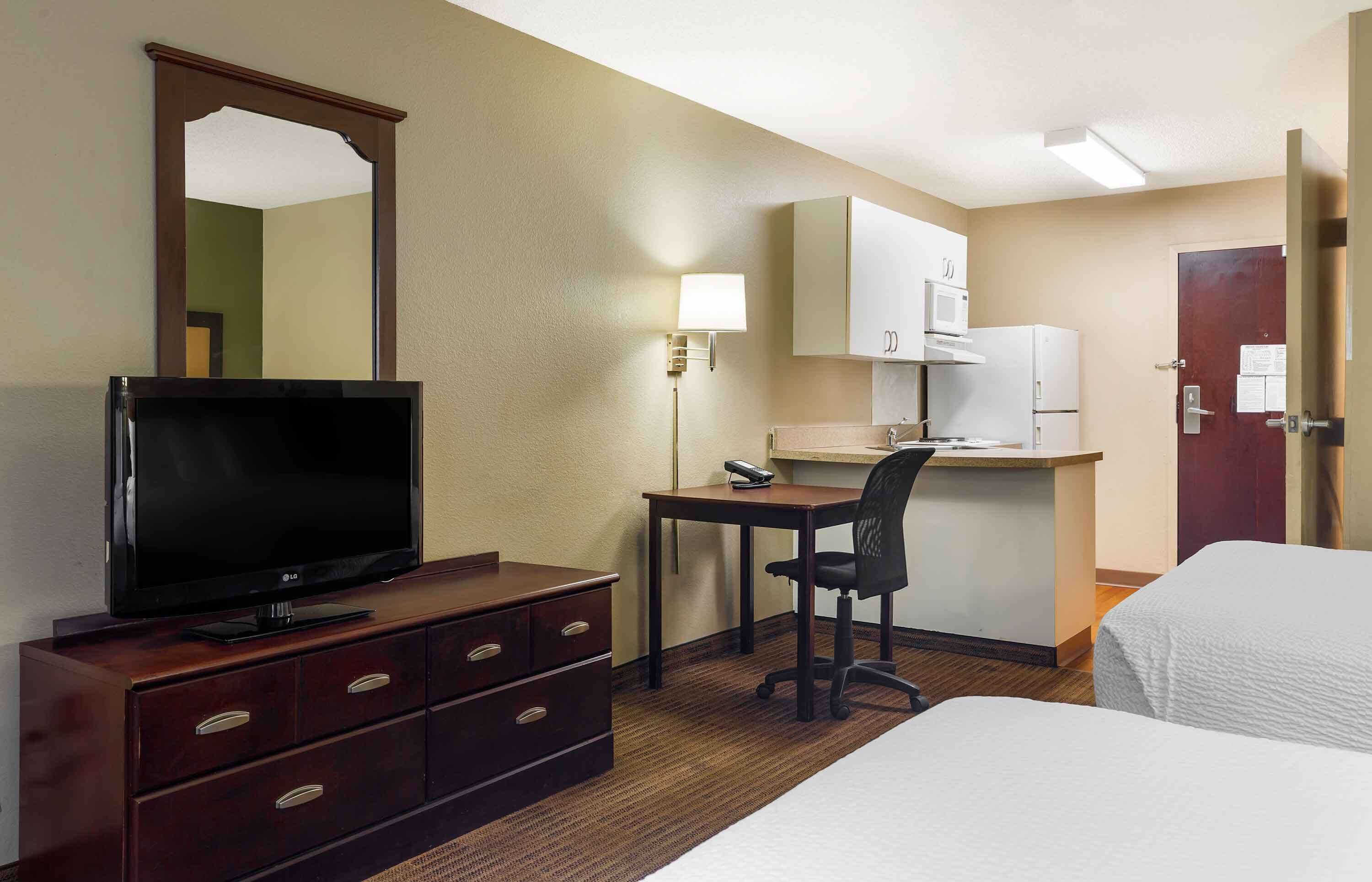 Une chambre d’hôtel équipée d’une télévision, d’un bureau, d’une chaise, d’une kitchenette et de deux lits.