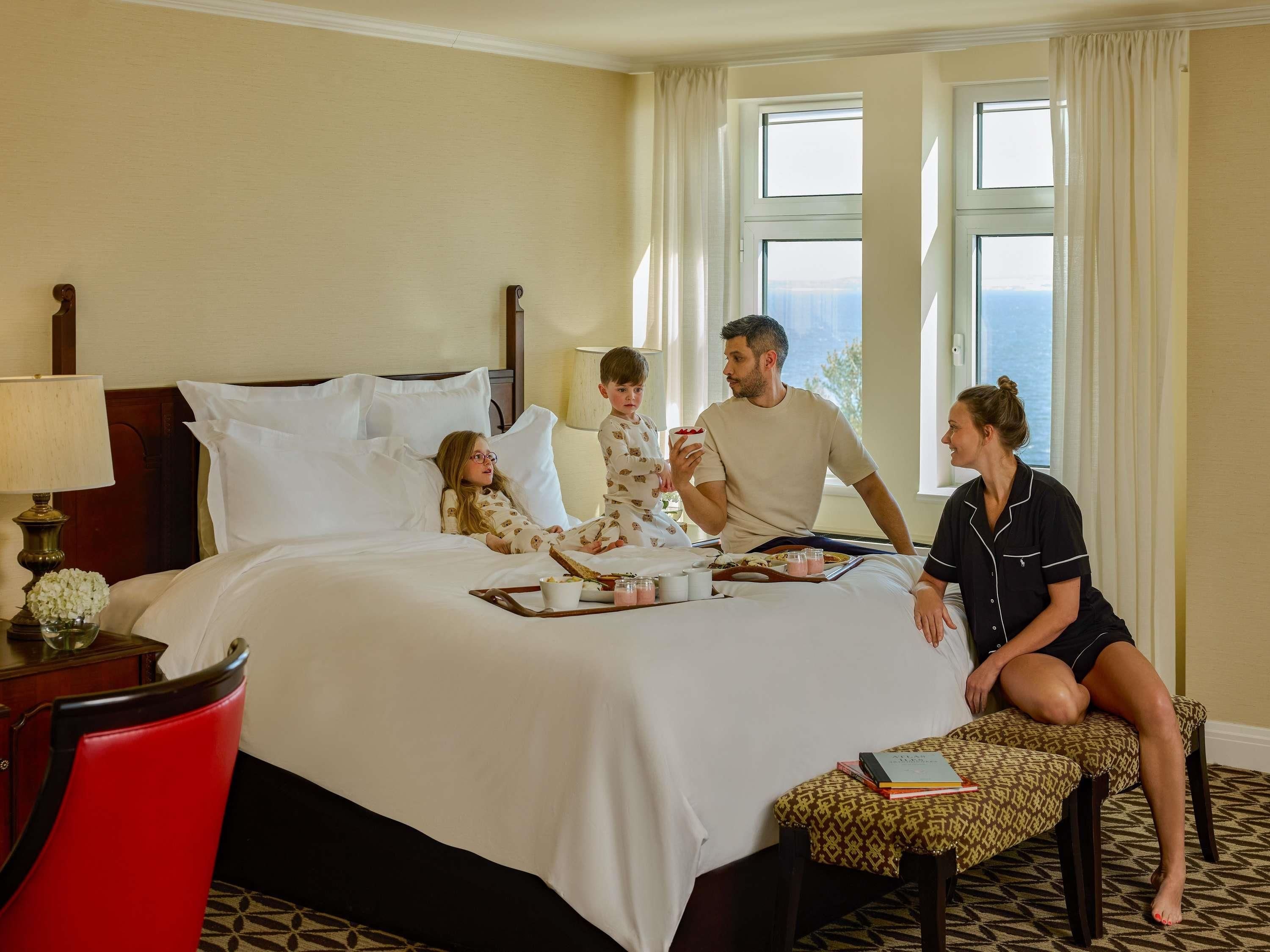 Habitación de hotel con cama, mesita de noche, lámpara y vistas al exterior por la ventana.
