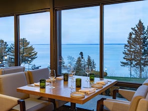 A dining table with chairs, set for a meal, overlooking a body of water and trees. - Fairmont Le Manoir Richelieu (La Malbaie)