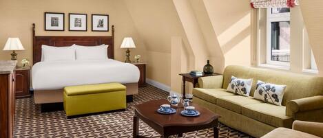 A hotel room with a bed, a sofa, a coffee table, a nightstand, and a window with a view.