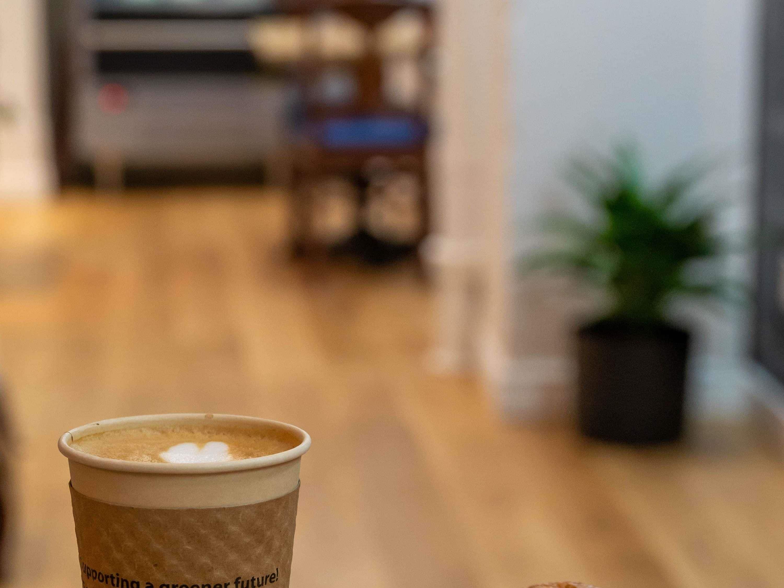 Une tasse de café avec un texte imprimé dessus, un plancher en bois, une chaise et une plante en pot.