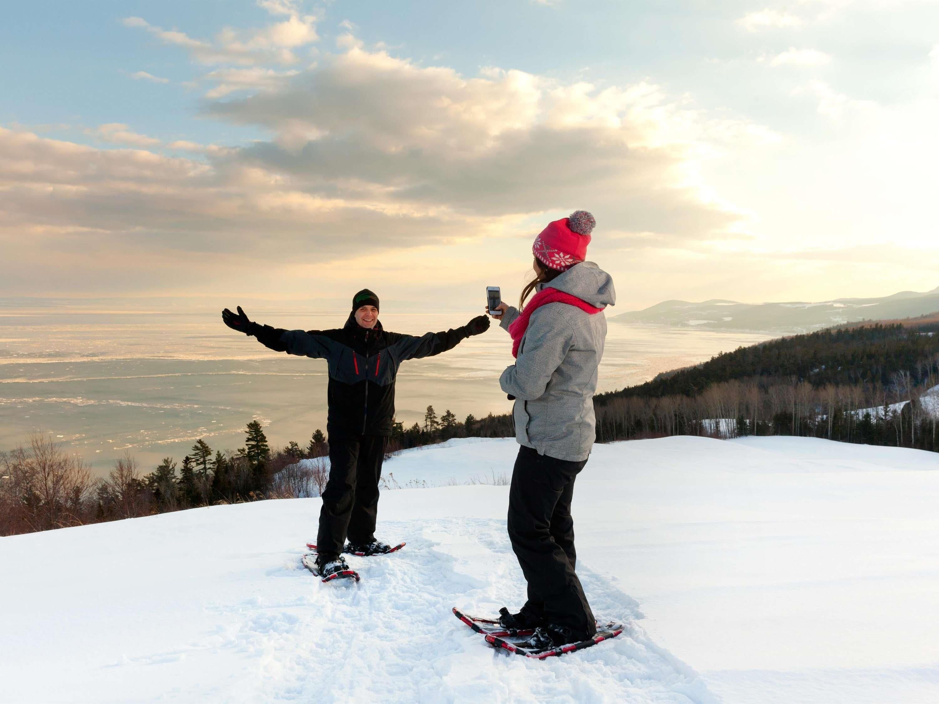 Two people on skis on a snowy hill with a view of a valley and mountains in the background.