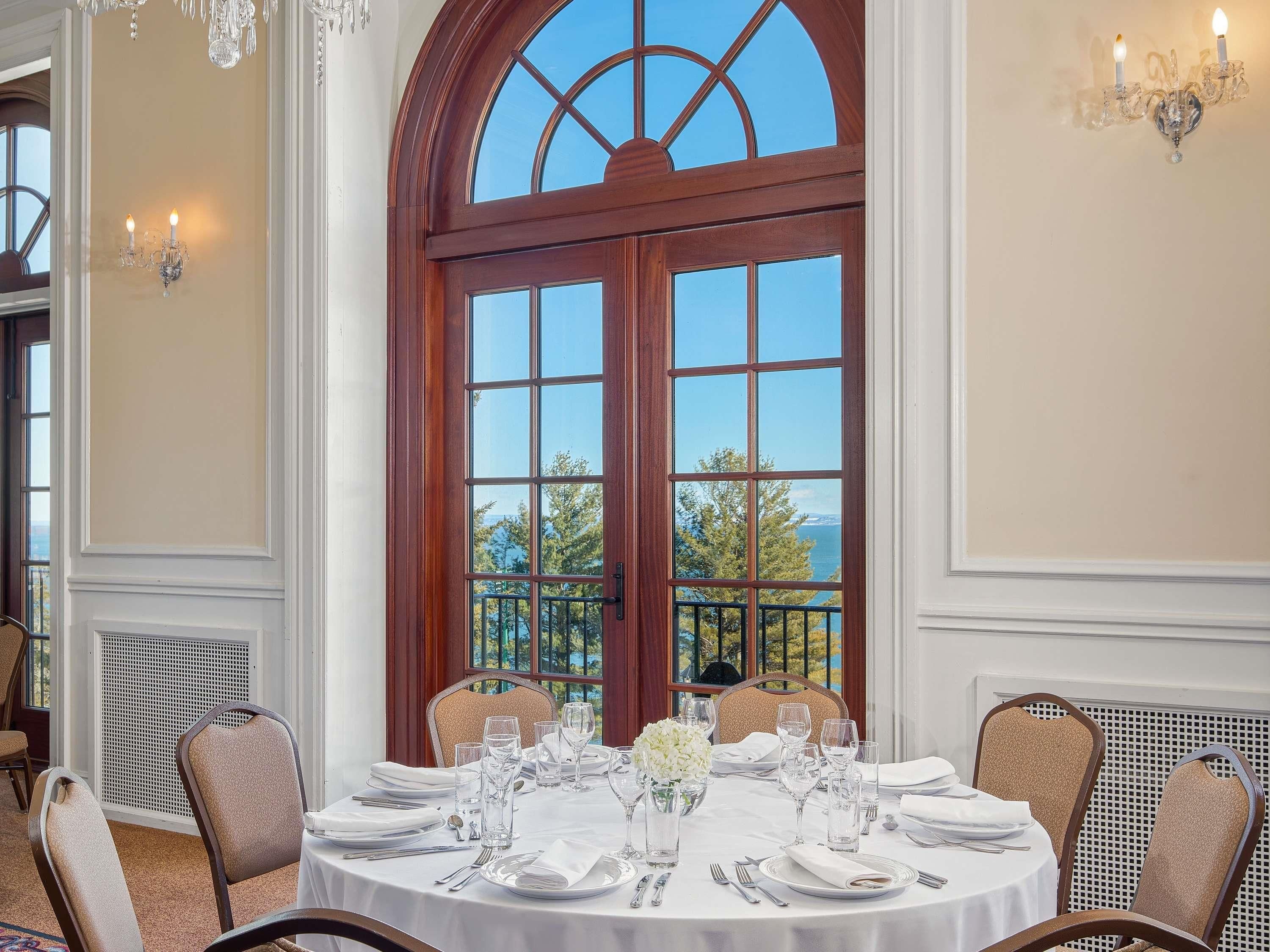 A dining room with a large bay window, a round table set for six, and a view of the outdoors.
