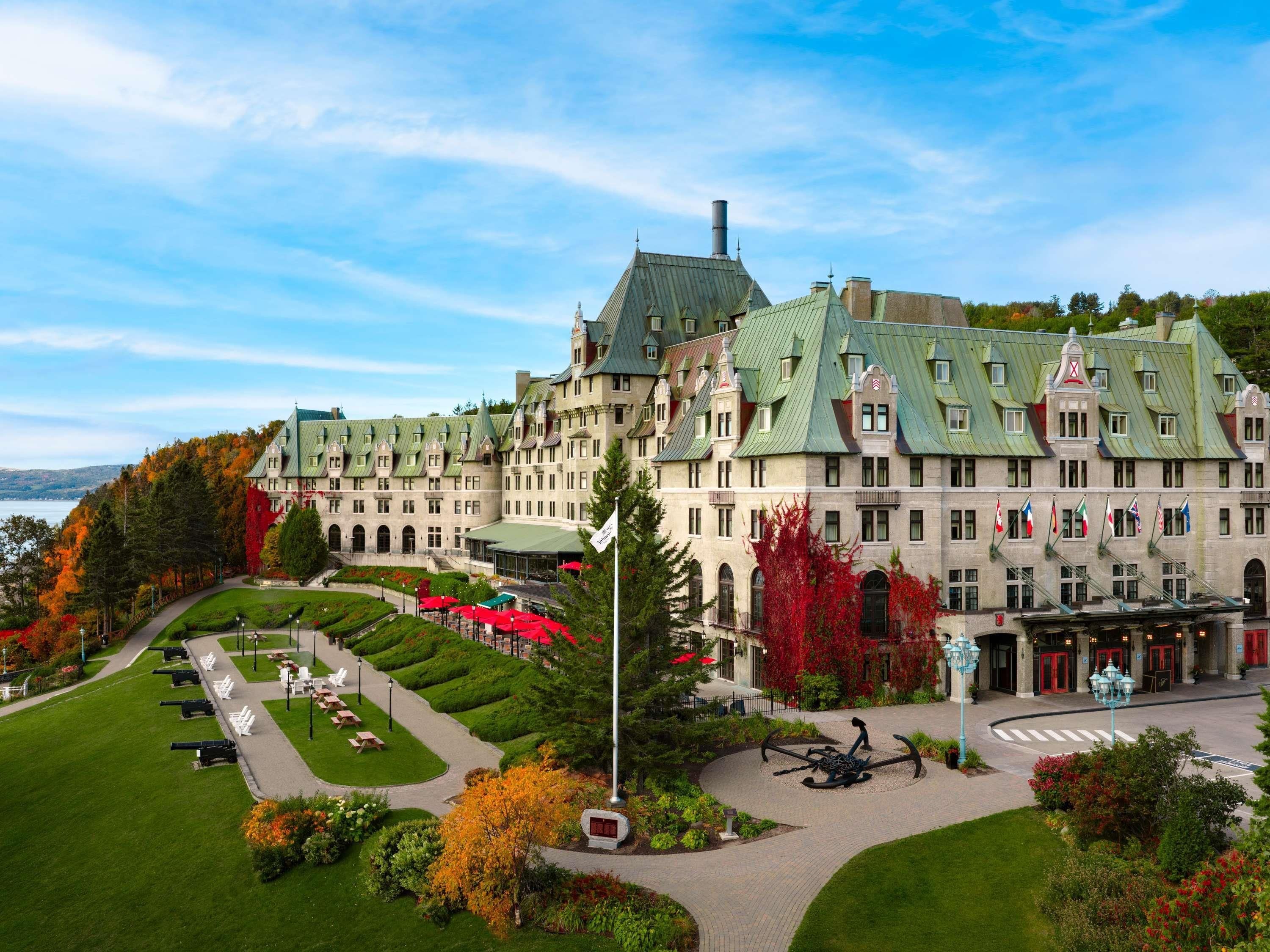 A large, historic hotel with a symmetrical facade, multiple chimneys, and a well-maintained garden with pathways and seating areas.