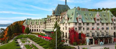 A large, historic hotel with a symmetrical facade, multiple chimneys, and a well-maintained garden with pathways and seating areas.