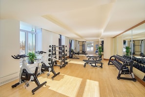 A gym with exercise equipment, large windows, and potted plants.