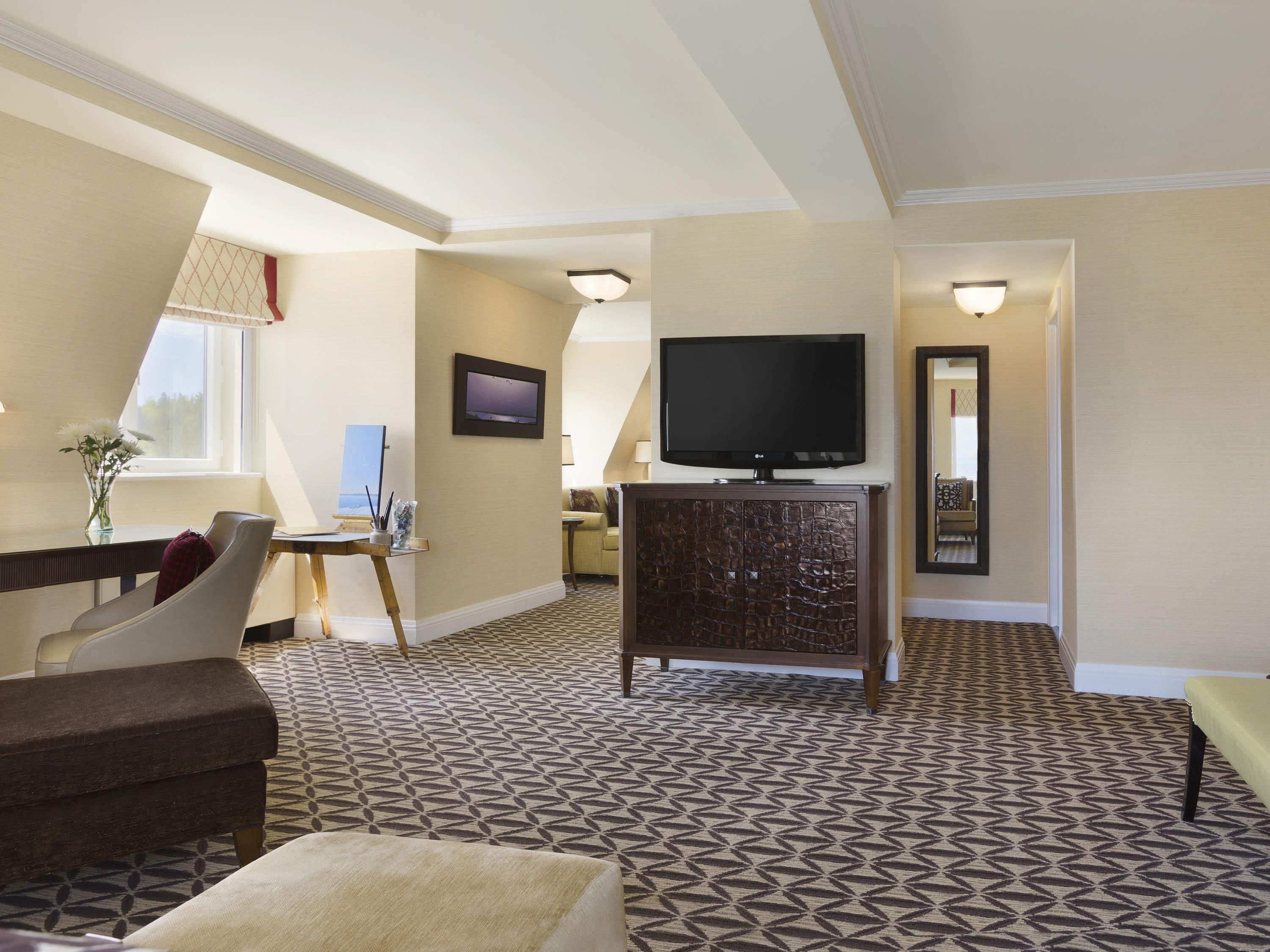Habitación de hotel con televisión, un cuadro, escritorio con un florero y alfombra estampada.