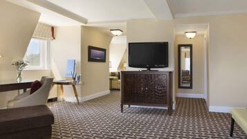 Habitación de hotel con televisión, un cuadro, escritorio con un florero y alfombra estampada.