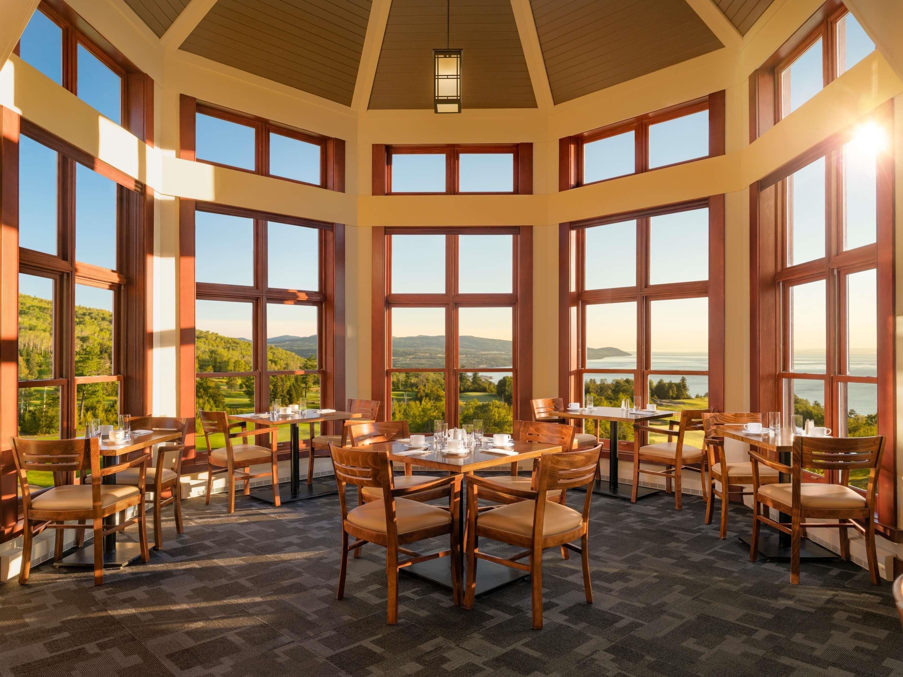 A dining area with large windows, wooden furniture, and a view of the landscape.