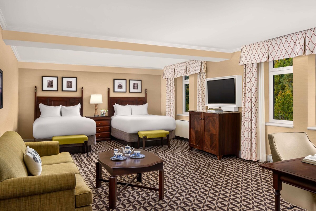 A hotel room with two beds, a TV, a desk, a chair, and a sofa.