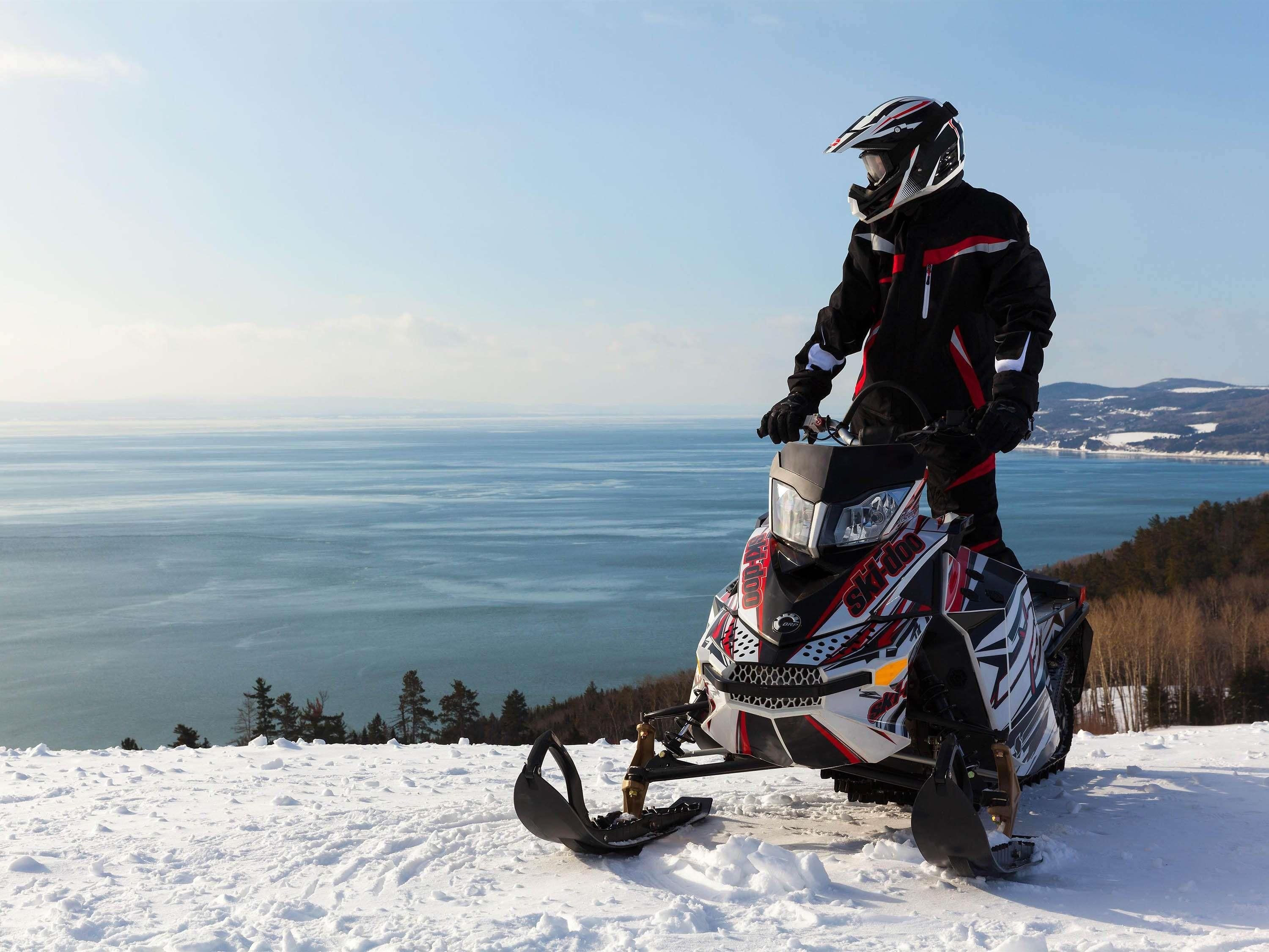 A snowmobile on a snowy landscape with a clear view of a lake and distant mountains.
