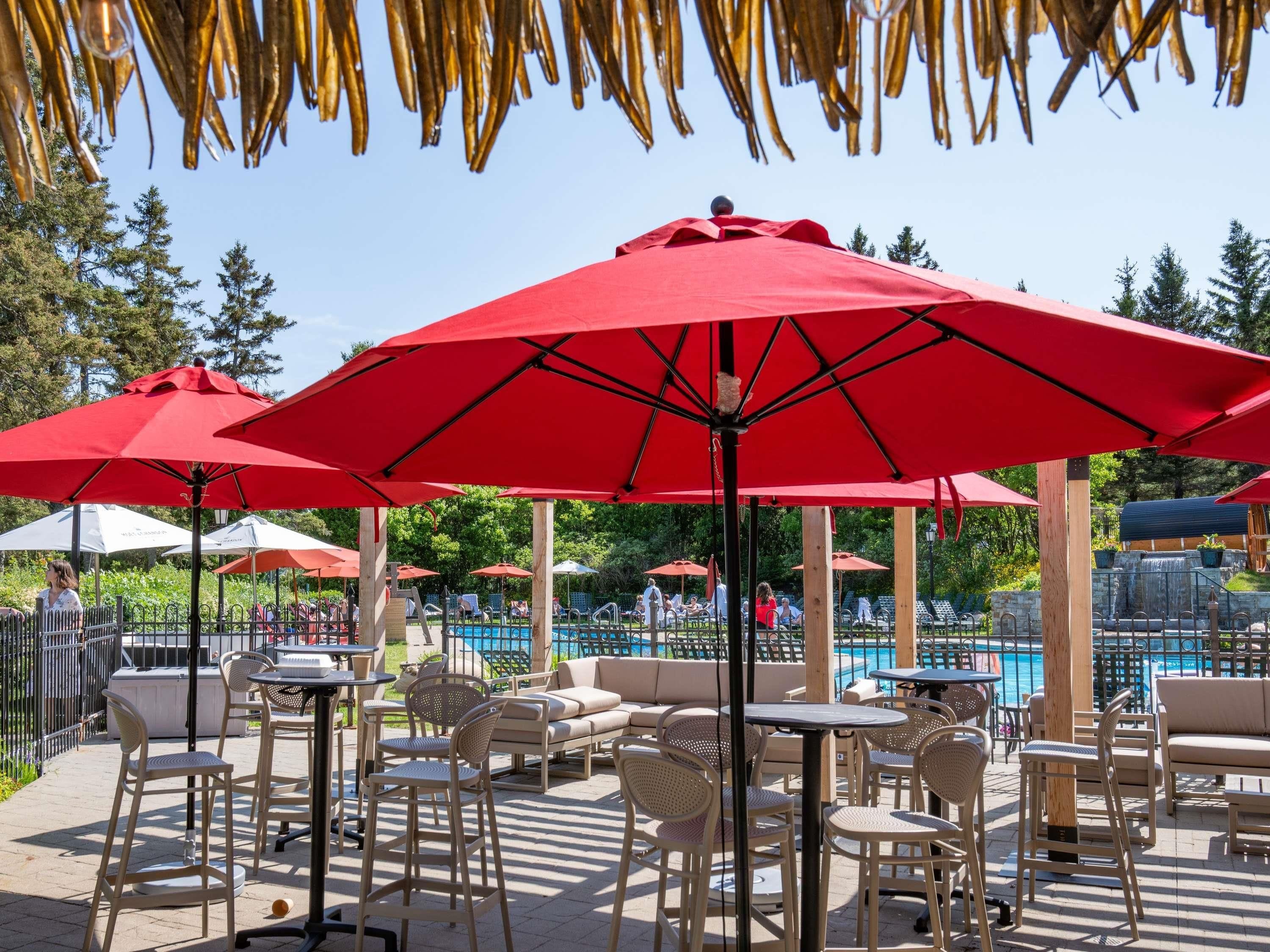 An outdoor patio with red umbrellas, wicker furniture, and a pool in the background.