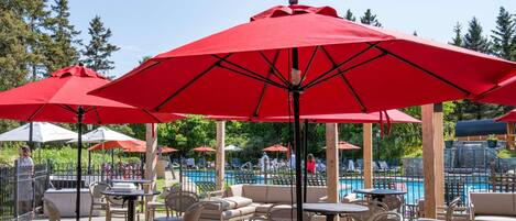 An outdoor patio with red umbrellas, wicker furniture, and a pool in the background.