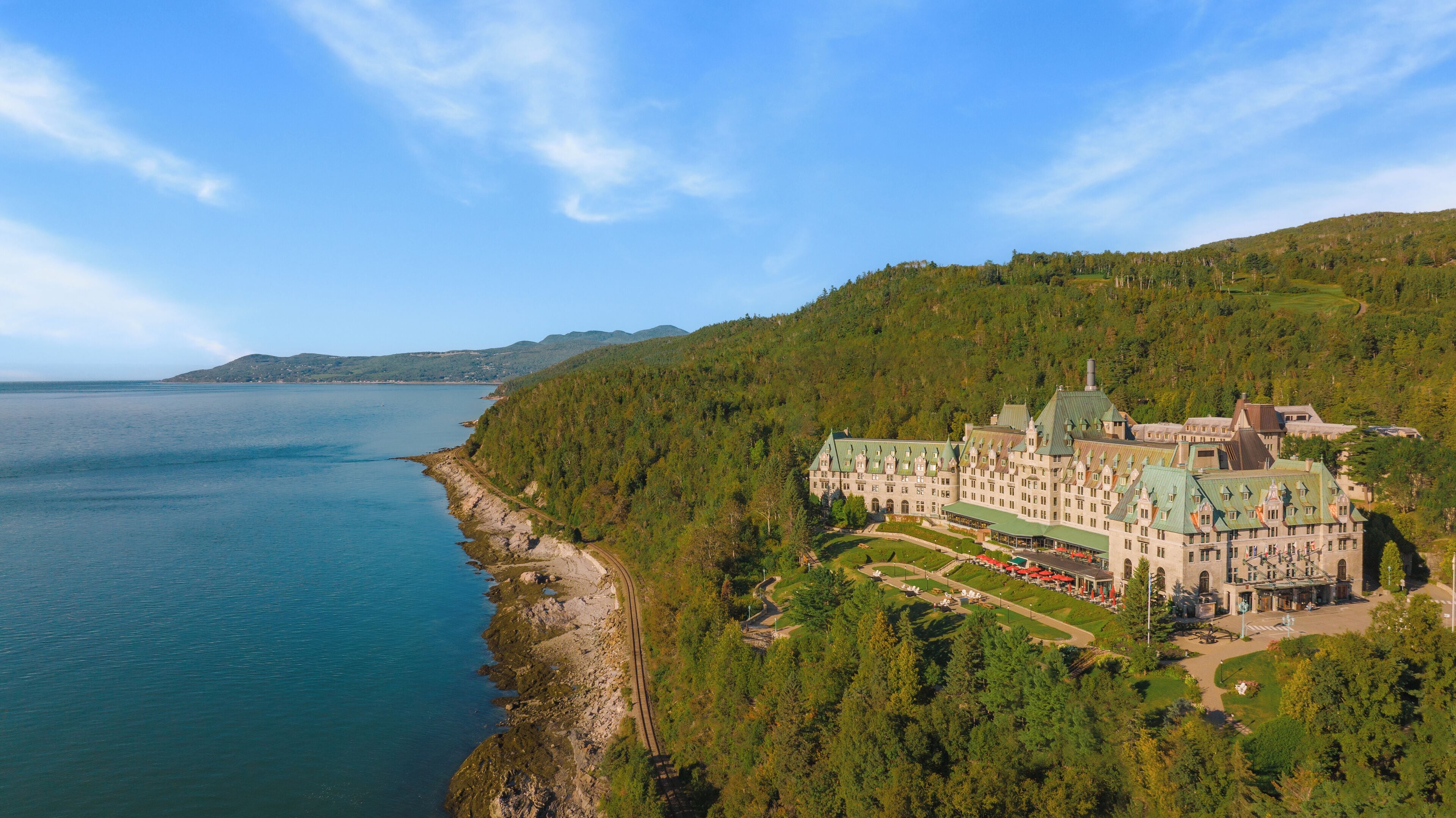 A large, historic building with a green roof, surrounded by lush greenery and a coastline.