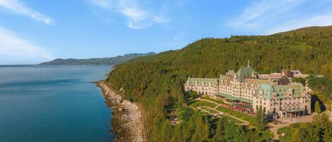 A large, historic building with a green roof, surrounded by lush greenery and a coastline.