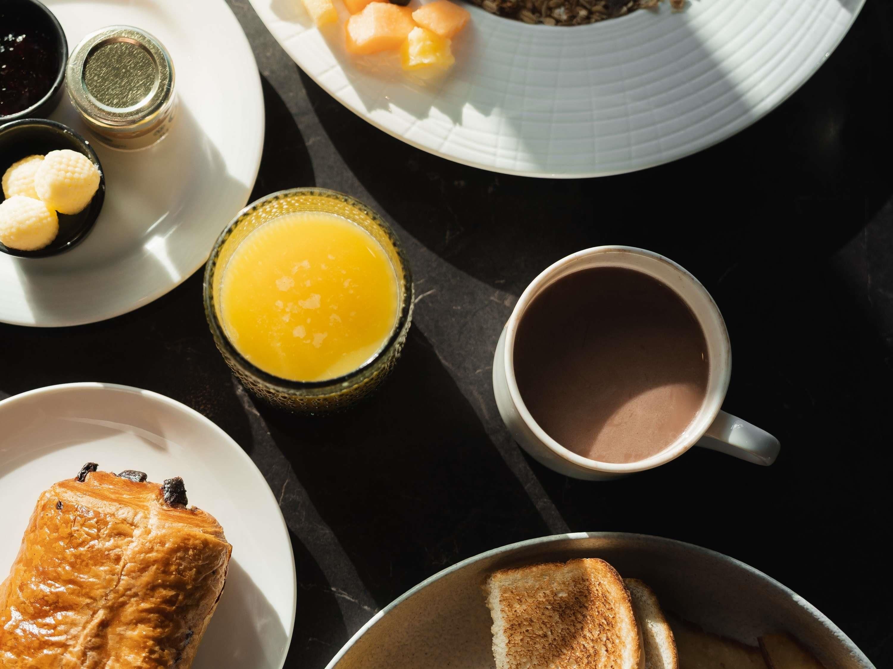 Een ontbijttafel met toast, een muffin, een glas jus d'orange, een kop koffie en een bord met fruit en ontbijtgranen.